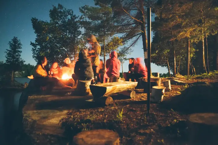 Campfire burning among trees as night falls over camp